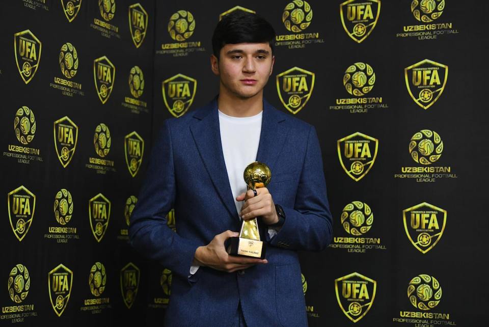 Man in suit holding a soccer award.