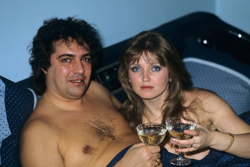 Linda Nolan and Brian Hudson in bed, toasting with champagne.