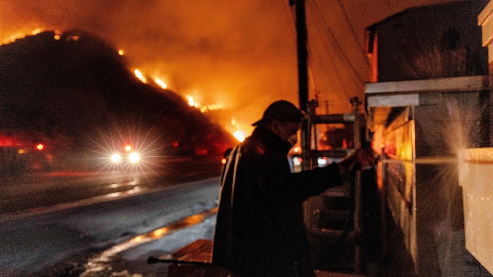 A Malibu resident waters his and his neighbor's homes during a wildfire.