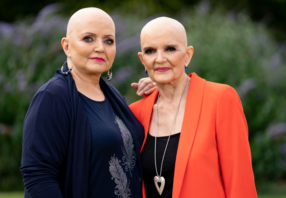 Two bald women stand together, one in a navy top and the other in an orange jacket.