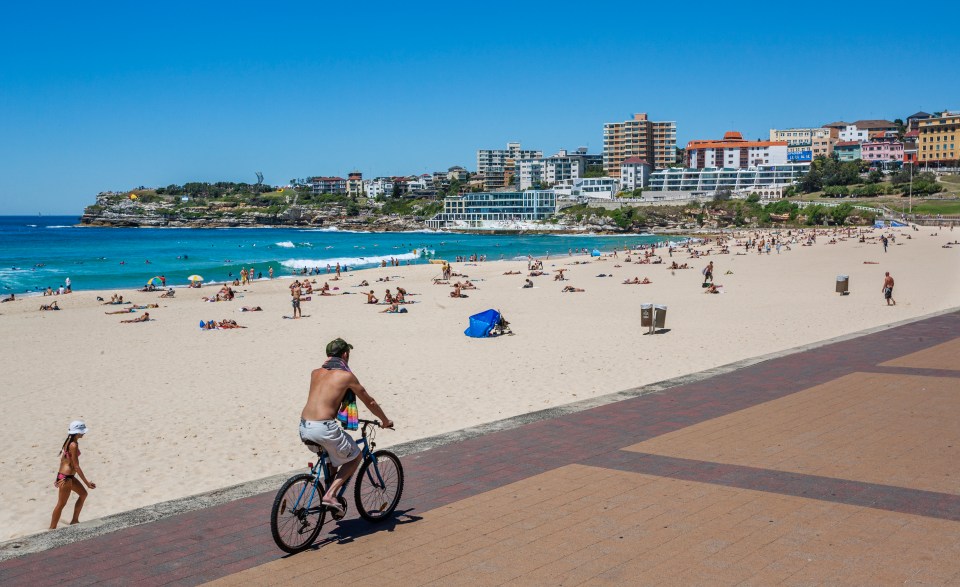 Bondi Beach in Sydney, Australia, with people sunbathing and a man cycling on the promenade.