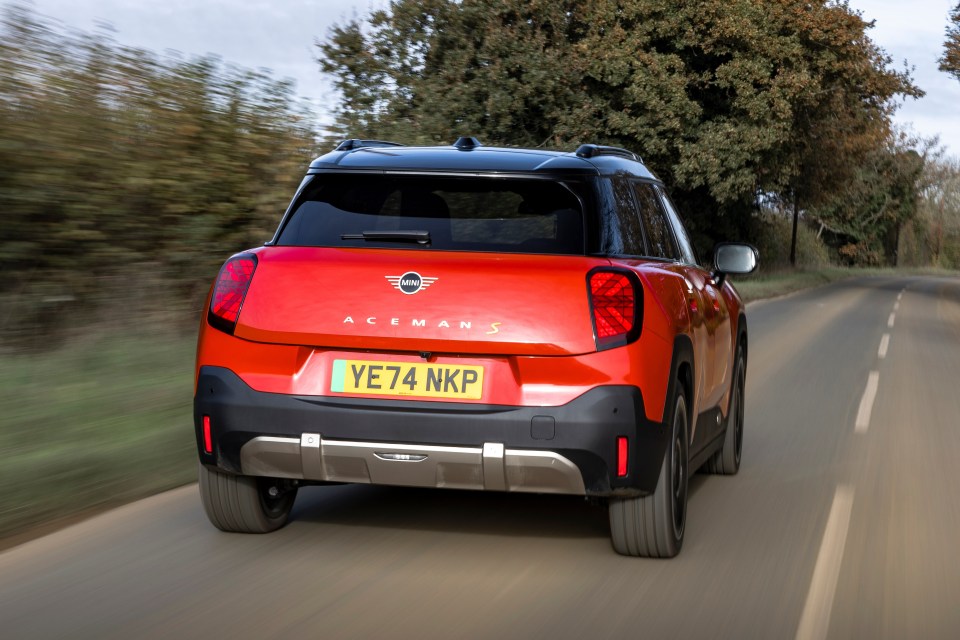 Rear view of a red Mini Aceman S driving down a country road.