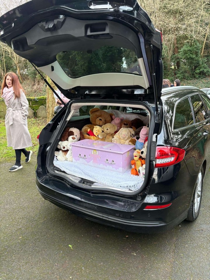 A baby's coffin surrounded by stuffed animals in the trunk of a car.