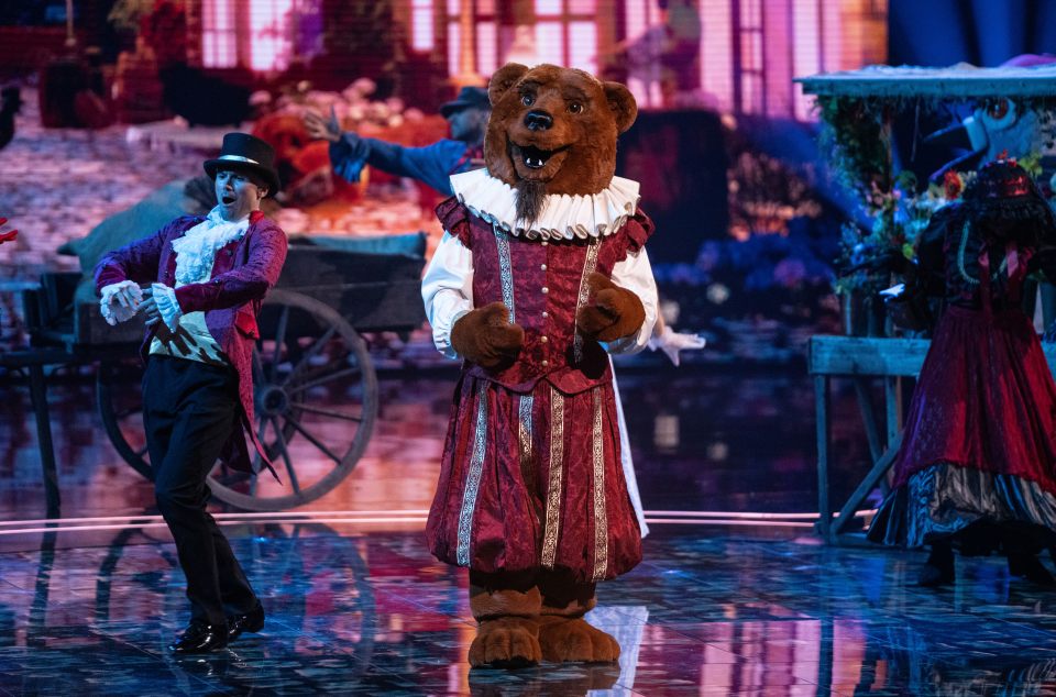 Bear in a red and gold costume on stage with a dancer.