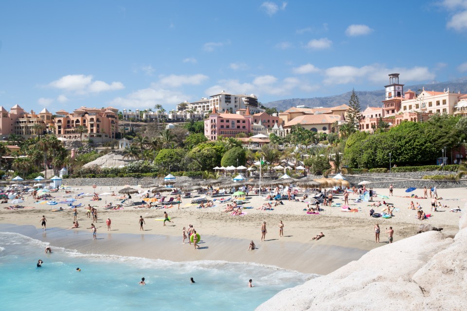 Crowded beach in Tenerife, Spain, with buildings in the background.