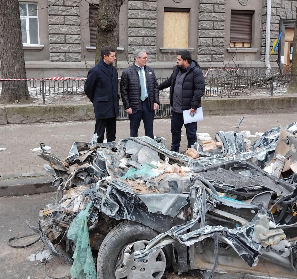 Three men standing near a severely damaged car.