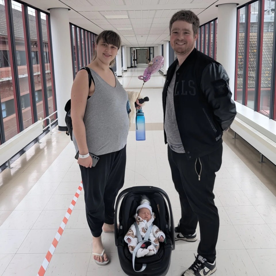 Parents holding their newborn baby in a car seat in a hospital hallway.