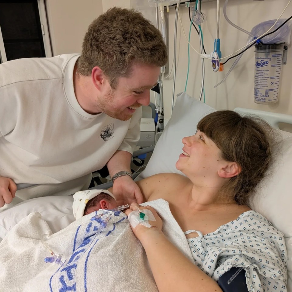 A new parent couple looks lovingly at their newborn baby in a hospital bed.