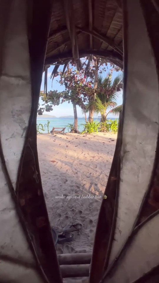 View from a hobbit hut doorway onto a sandy beach and ocean.