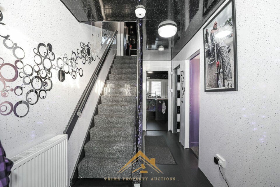 Interior view of a home's hallway with black walls, grey carpeting, and a staircase.