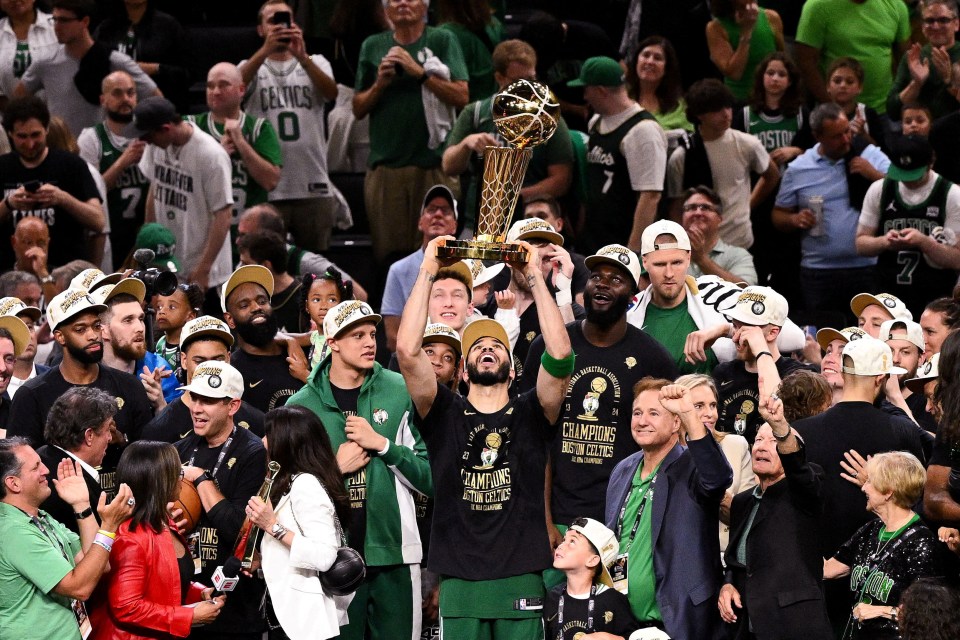 Jayson Tatum holding the Larry O'Brien Championship Trophy with the Boston Celtics team.