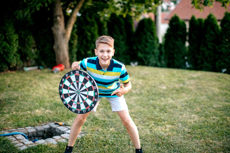 Boy holding a dartboard outdoors.