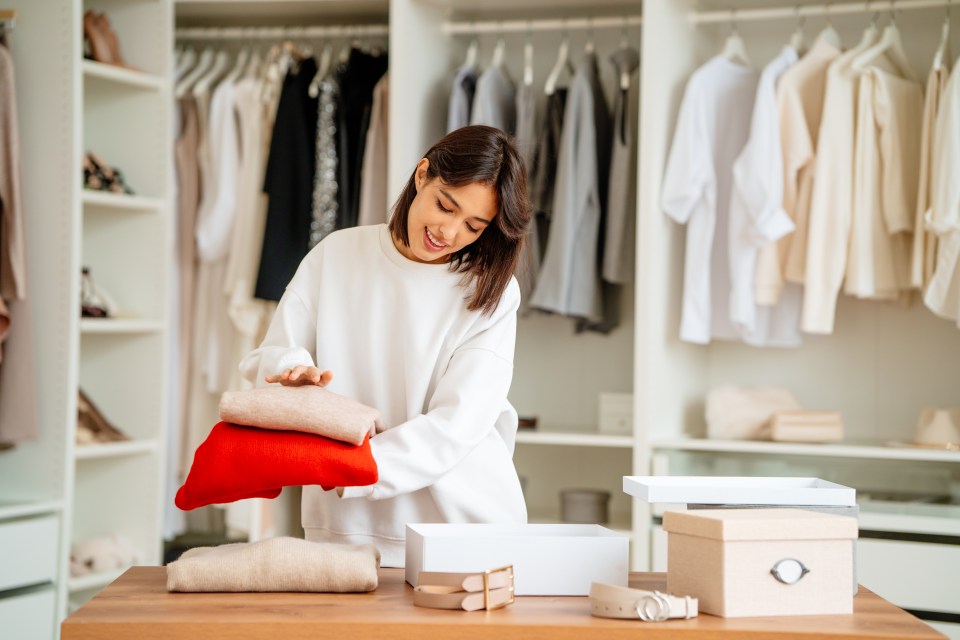 Woman packing sweaters into boxes in a walk-in closet.