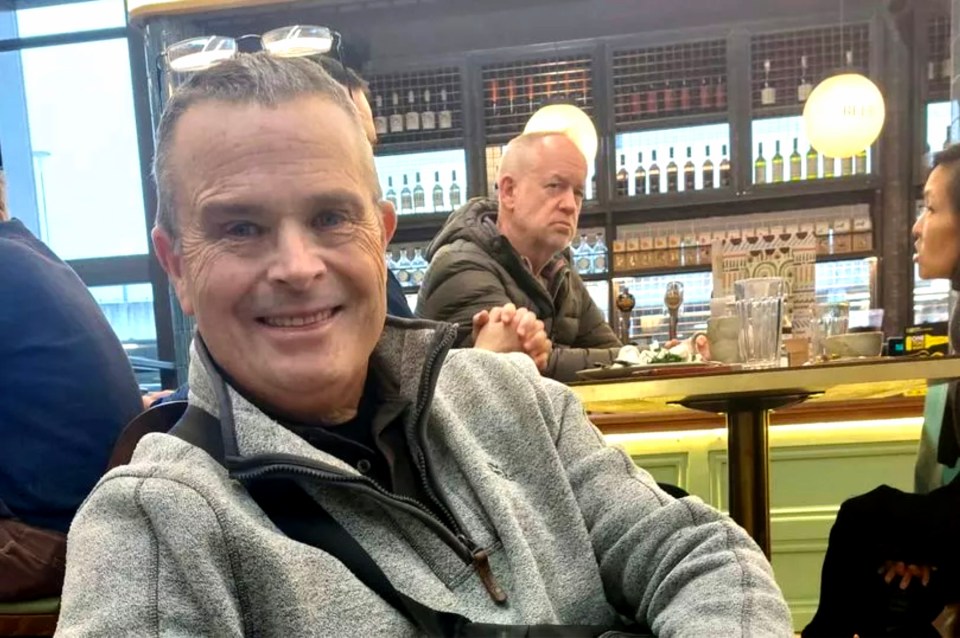 A man smiling at the camera, sitting at a bar.