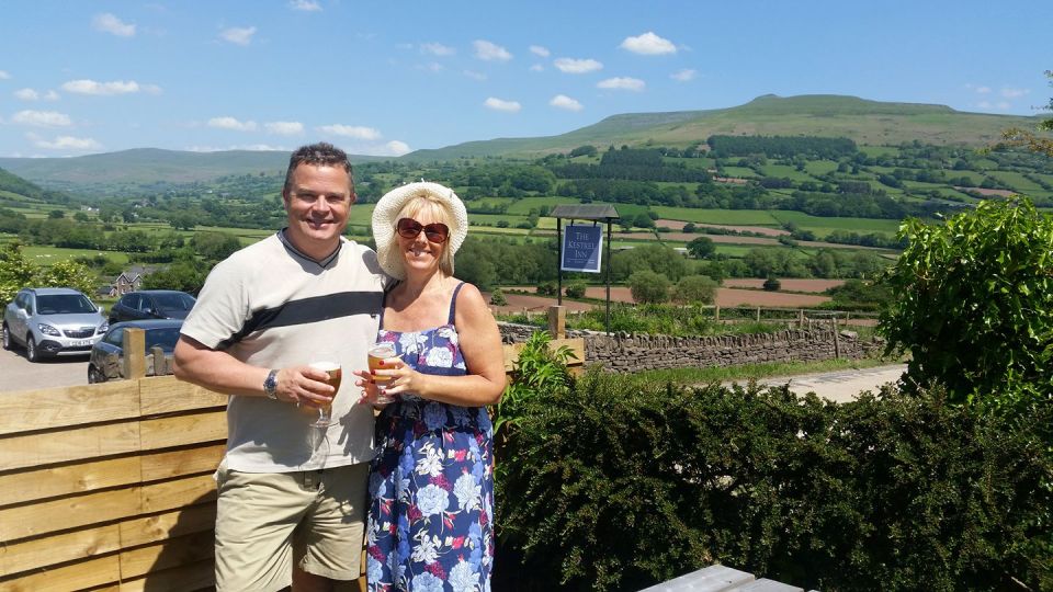 Couple enjoying drinks outside a pub with a scenic view.