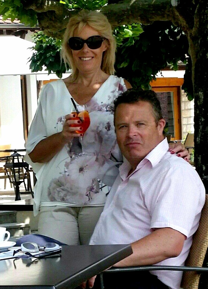 A man and woman sitting at an outdoor table; the woman holds a cocktail.