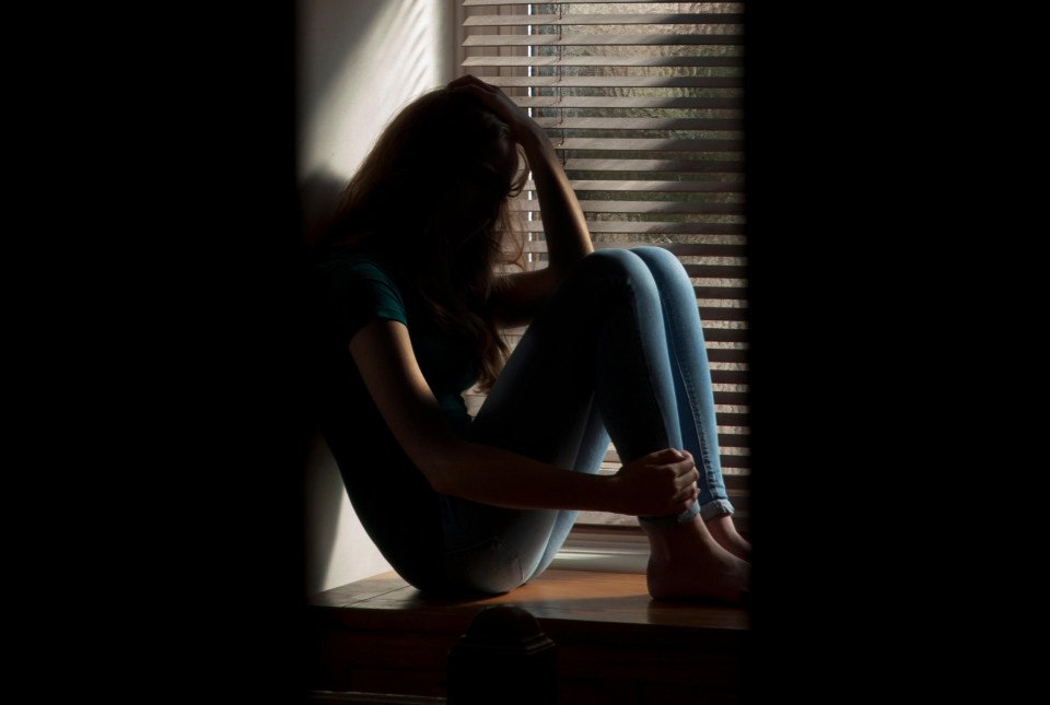 Teenage girl sitting by a window, head in hands.