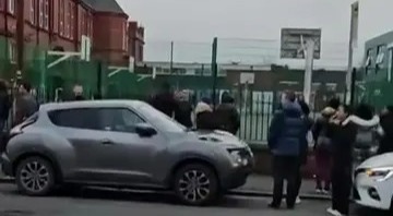 People gathered outside a school building near parked cars.