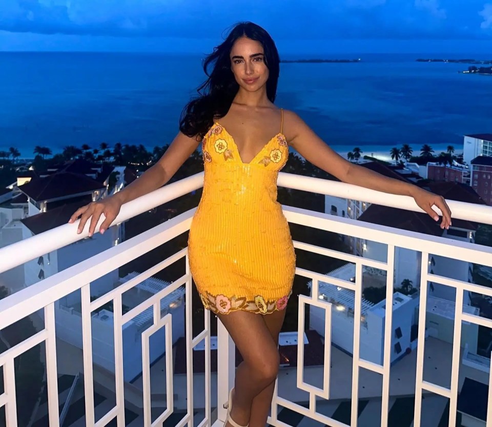 Woman in yellow dress on balcony overlooking ocean at dusk.