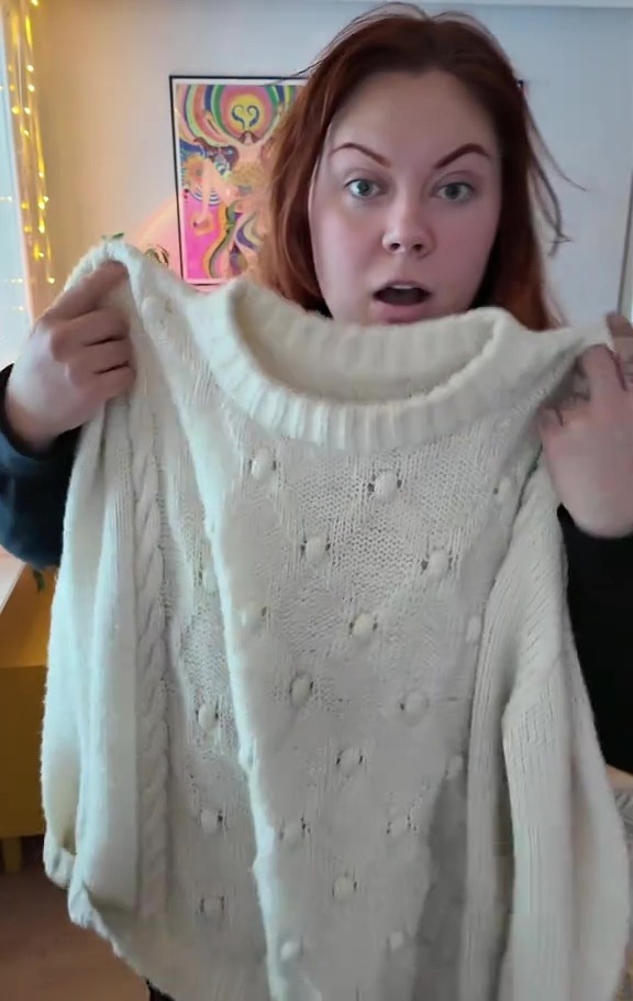 Woman holding up a cream-colored sweater.