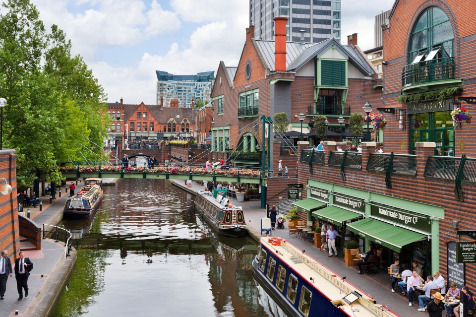 Narrowboats moored along a canal in Birmingham, next to restaurants and shops.