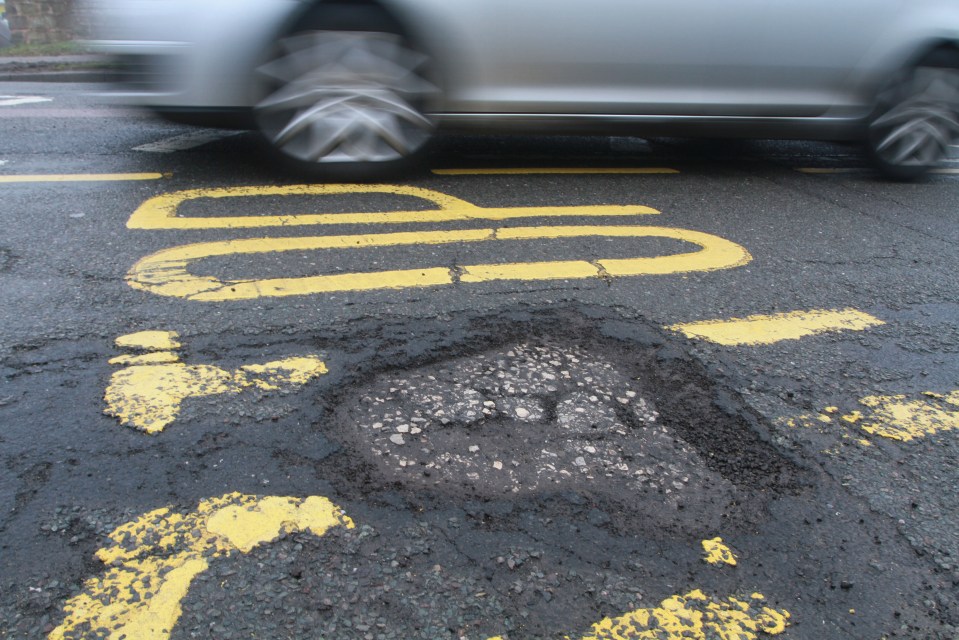 Car driving past a pothole in the road.