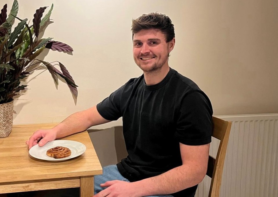 Man sitting at a table with a cinnamon roll on a plate.