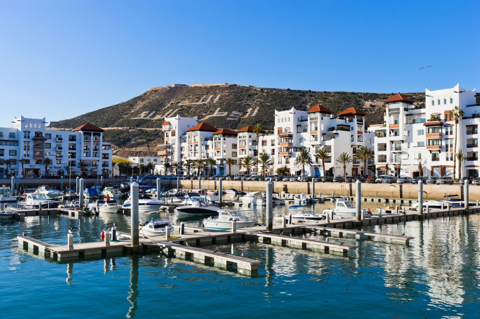 Agadir marina with boats docked and buildings on a hill.