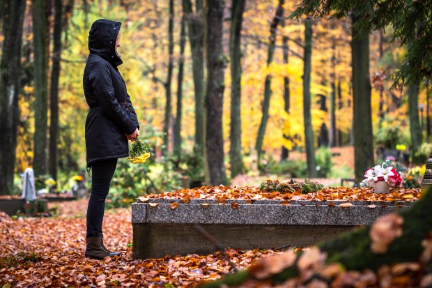 Woman mourning at a gravesite in an autumn cemetery.