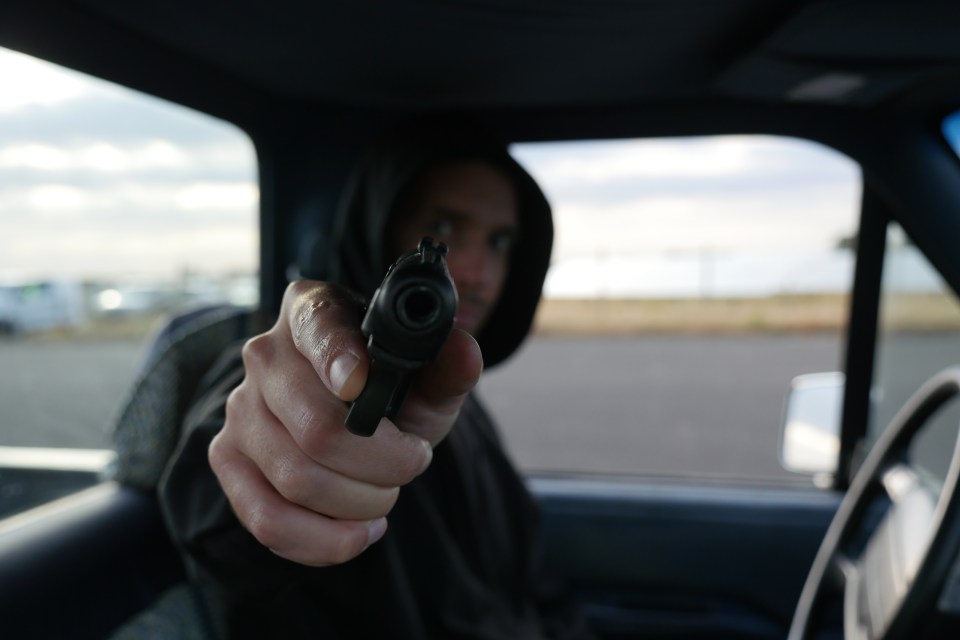 Illustration of a person pointing a gun from inside a vehicle.