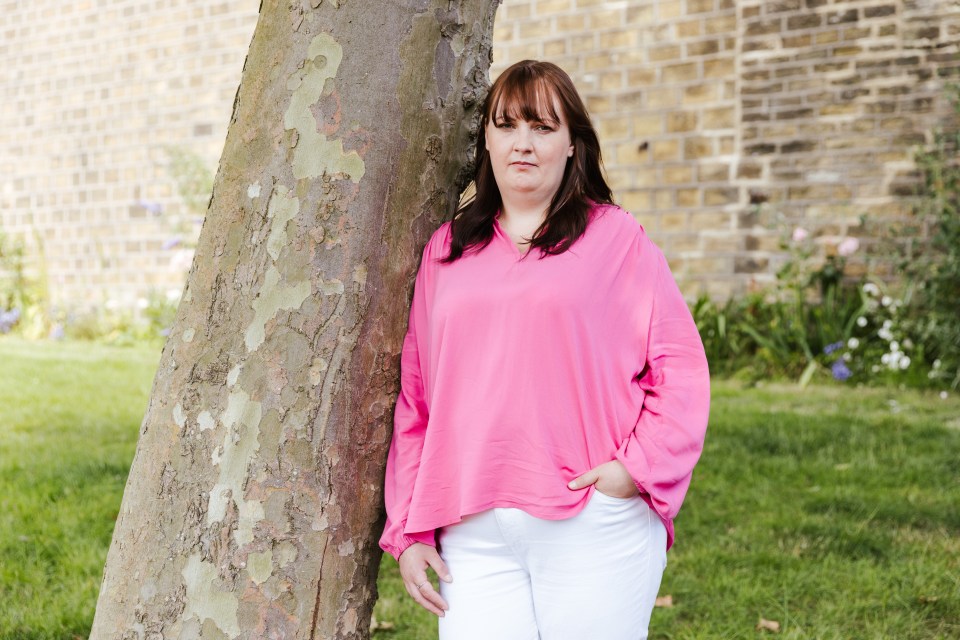 Woman in pink shirt leaning against a tree.