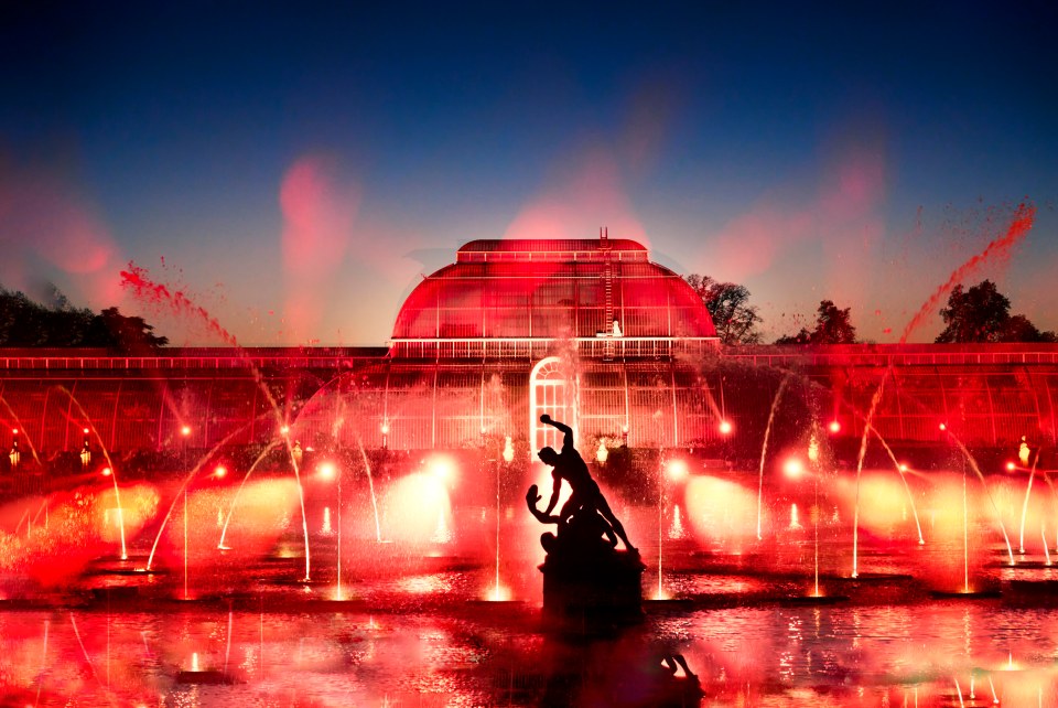 Kew Gardens Palm House illuminated in red with water fountains.