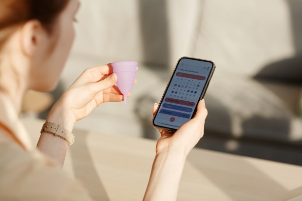 Woman using a period tracking app and holding a menstrual cup.