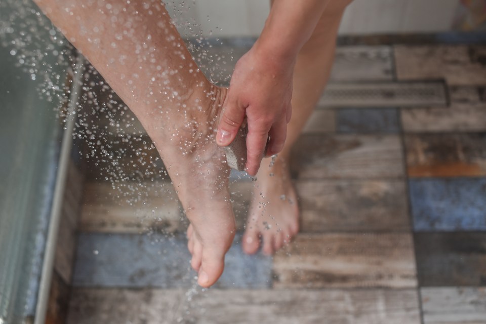 Woman using a pumice stone to exfoliate her foot in the shower.