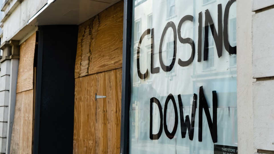 Boarded-up shop window with "Closing Down" painted on it.