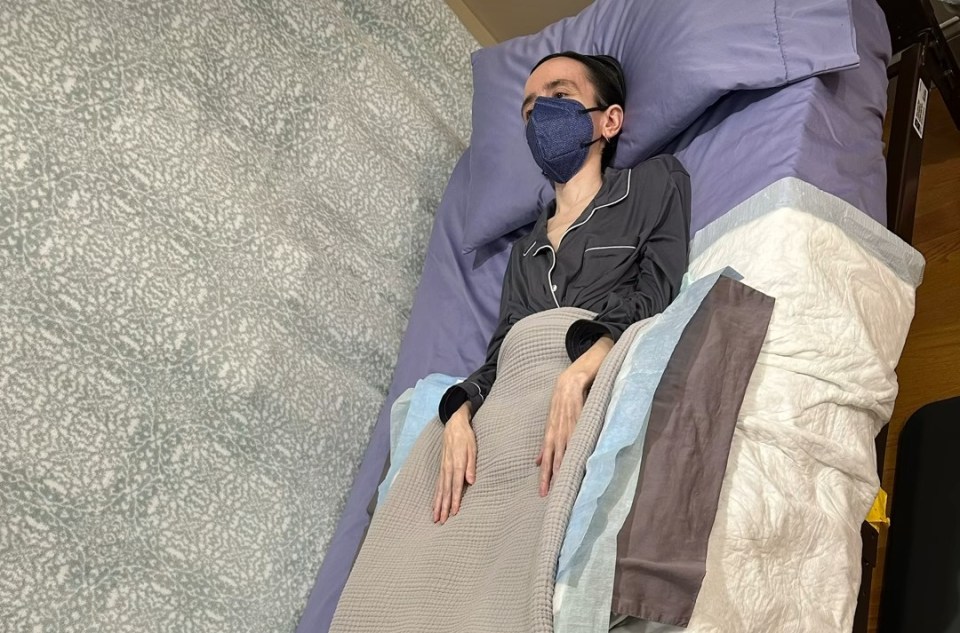 Woman in pajamas lying in bed wearing a face mask.