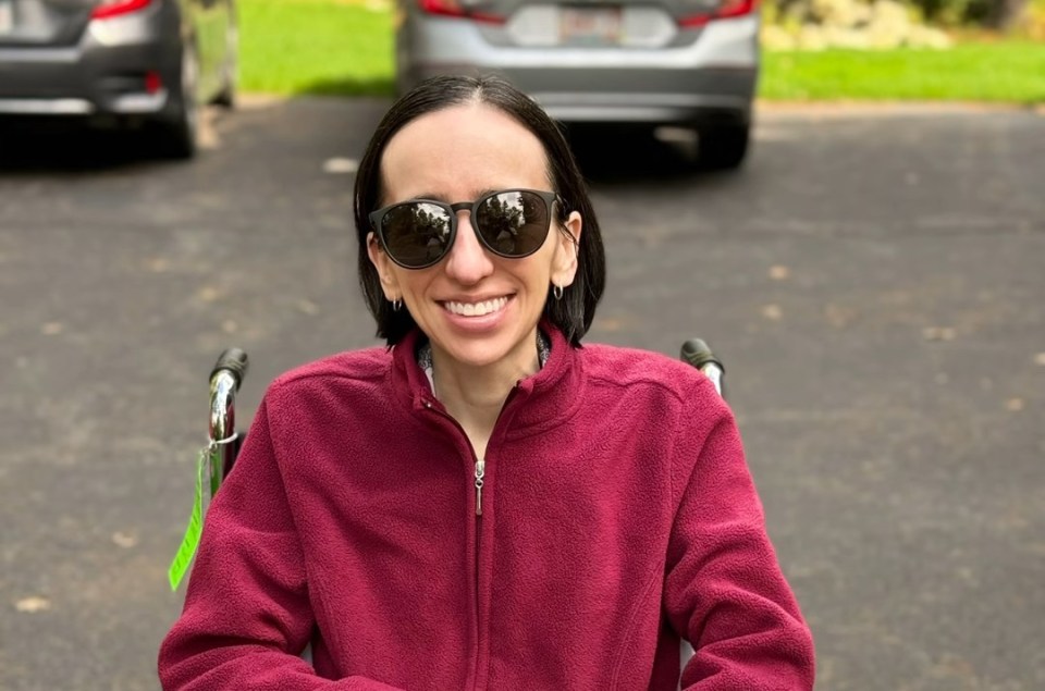 Woman in wheelchair wearing sunglasses and a maroon fleece.