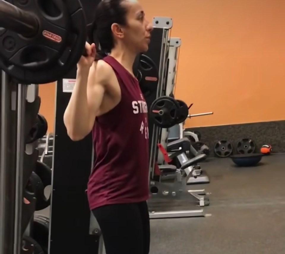 Woman performing a barbell back squat in a gym.