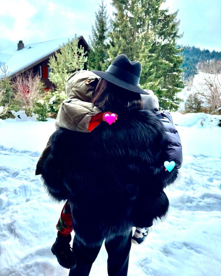 Woman in a fur coat carrying two children in the snow.