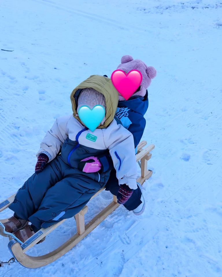 Two toddlers on a sled in the snow.