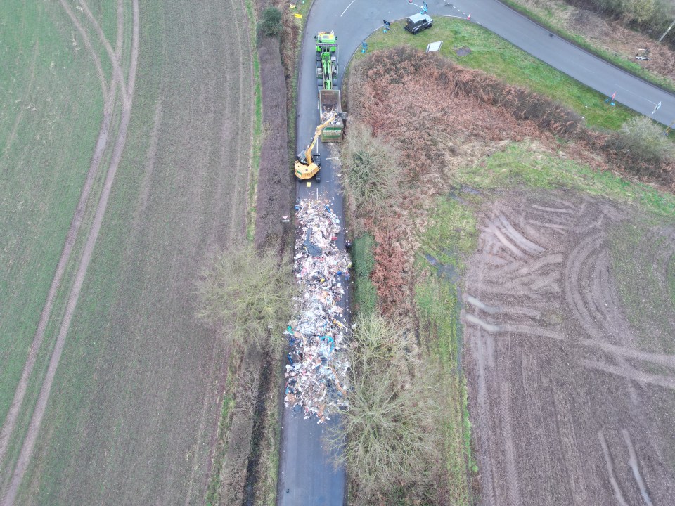 Aerial view of contractors removing a large pile of fly-tipped waste from a road.