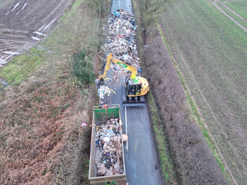 Aerial view of a digger removing a large pile of fly-tipped waste from a road.