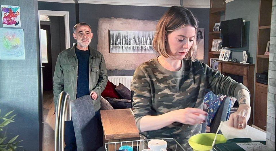 Scene from Coronation Street showing a woman in camouflage preparing food while a man stands in the background.