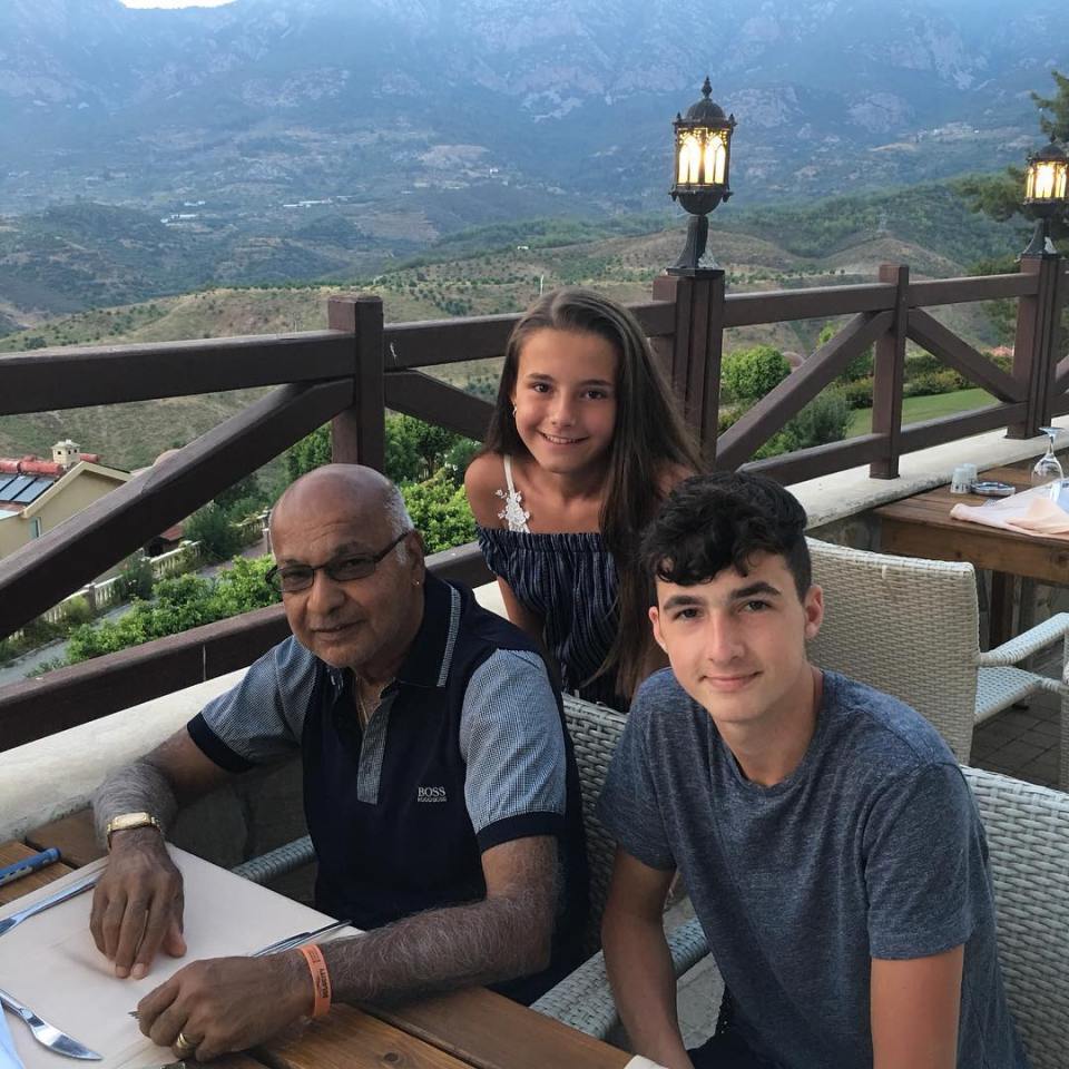 A man and two teenagers sit at an outdoor table overlooking a mountain range.