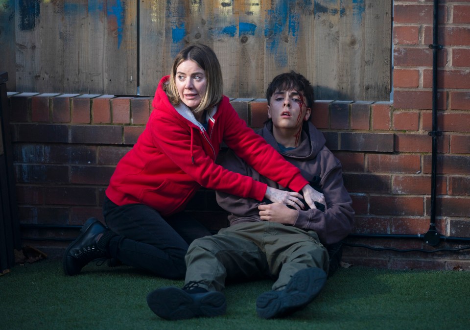 A woman comforts a bleeding teenage boy sitting on the ground.