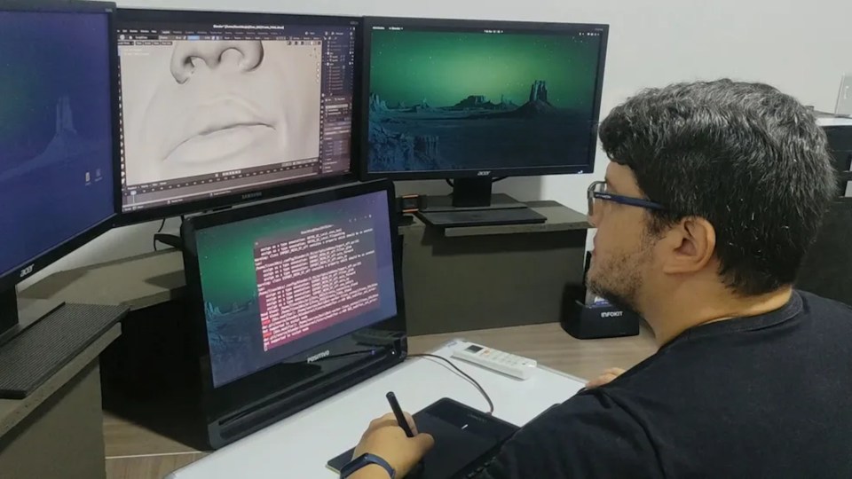 Man using a graphics tablet and multiple monitors to create a 3D model of a face.