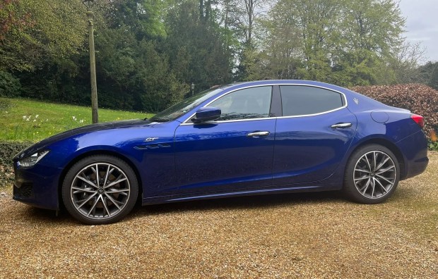 Blue Maserati Ghibli parked in a gravel driveway.