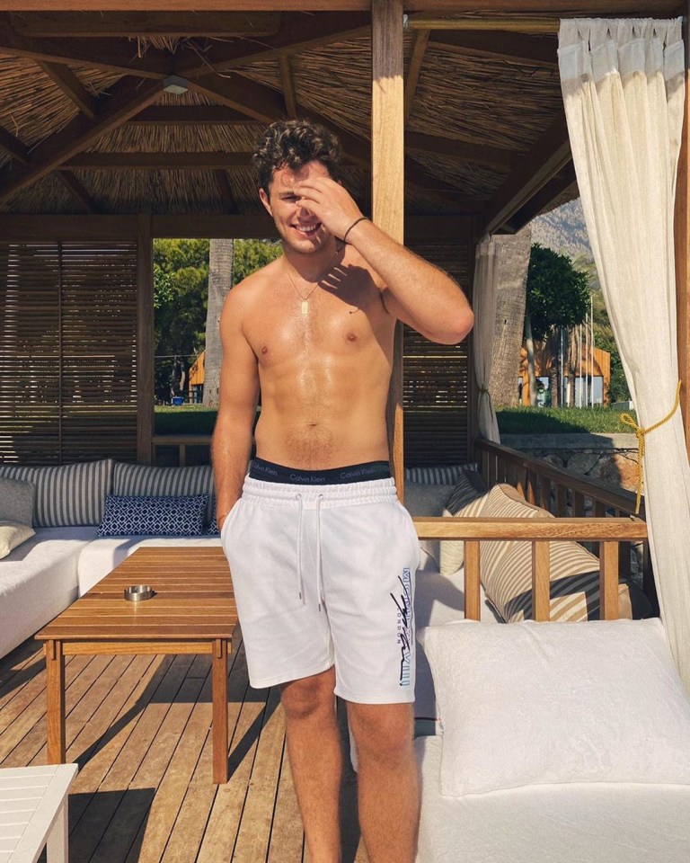 Shirtless man in white shorts smiling in a beach cabana.