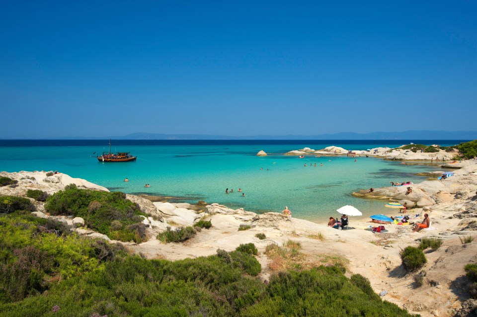 Beach scene in Halkidiki, Greece with turquoise water, people swimming and relaxing on the shore.