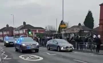 Police cars driving on a street with a crowd of people.